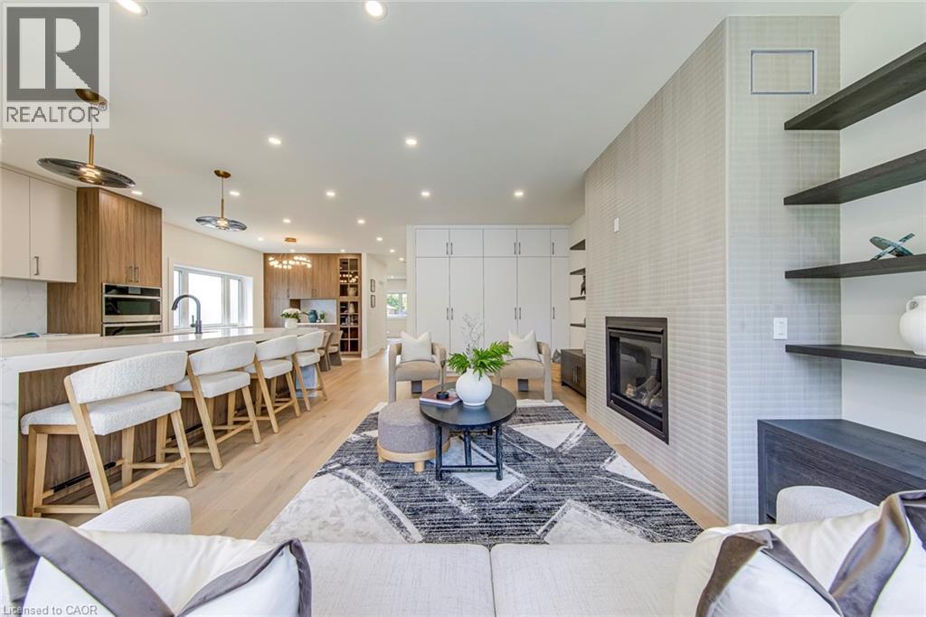 Open-concept living area featuring a modern fireplace with a tiled surround, light wood-finish flooring, recessed lighting, and a kitchen island with seating - 1411 Mountain Grove Avenue, Burlington, ON - Indoor Photo Showing Living Room With Fireplace