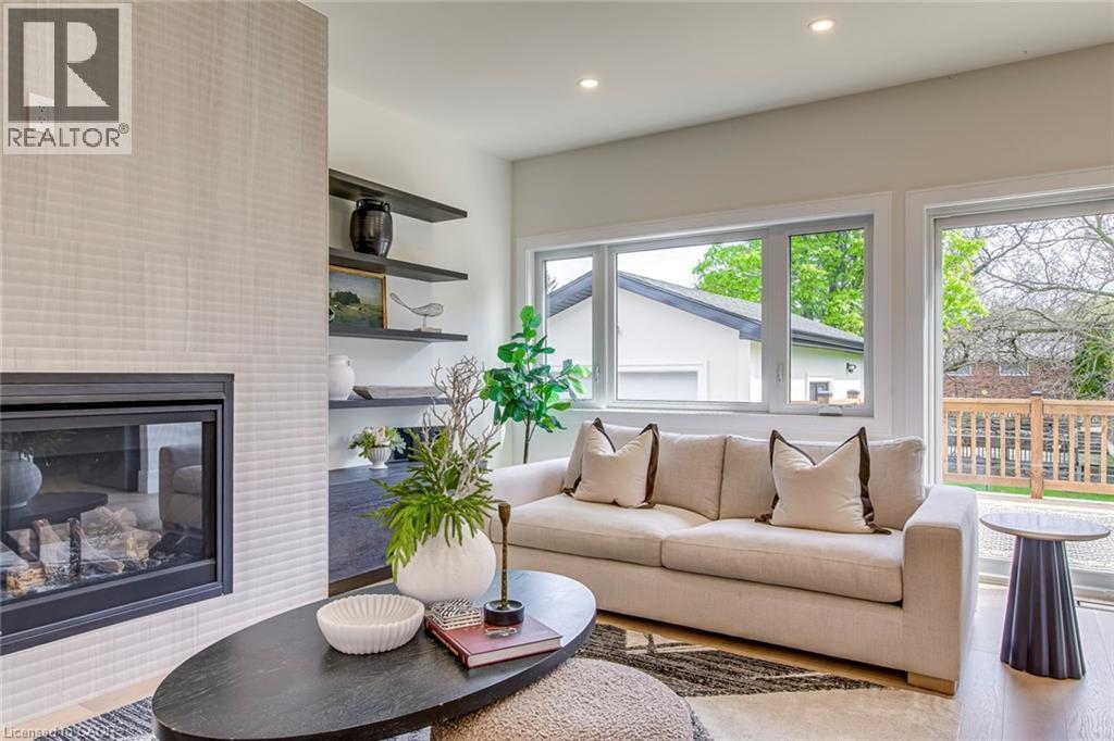 Living room featuring a fireplace with a textured surround, built-in shelving, recessed lighting, and large windows overlooking a wood deck - 1411 Mountain Grove Avenue, Burlington, ON - Indoor Photo Showing Living Room With Fireplace