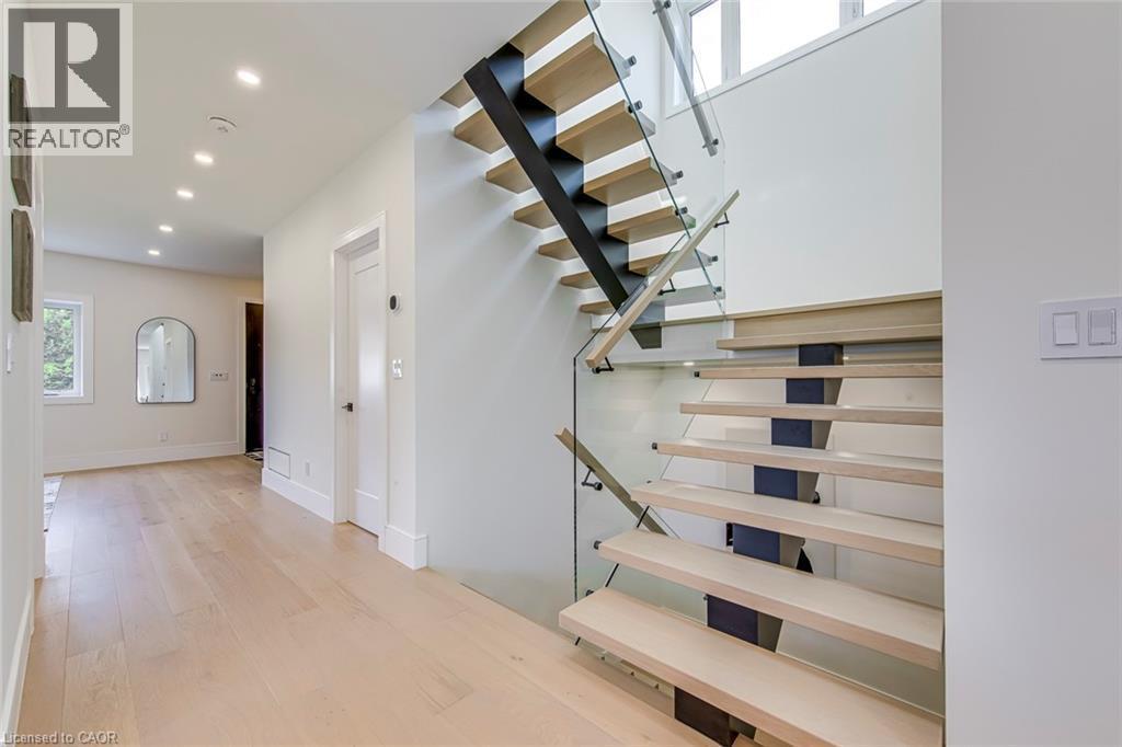 Contemporary open-riser staircase featuring wood-finish treads, a black metal spine, and glass panel railings - 1411 Mountain Grove Avenue, Burlington, ON - Indoor Photo Showing Other Room