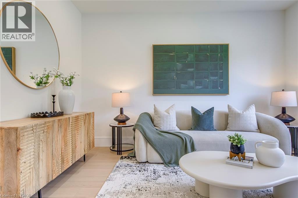 Bright living space featuring light wood-finish flooring, a contemporary decorative mirror with a gold-tone frame, a light-toned area rug, and a modern console table with textured wood doors - 1411 Mountain Grove Avenue, Burlington, ON - Indoor