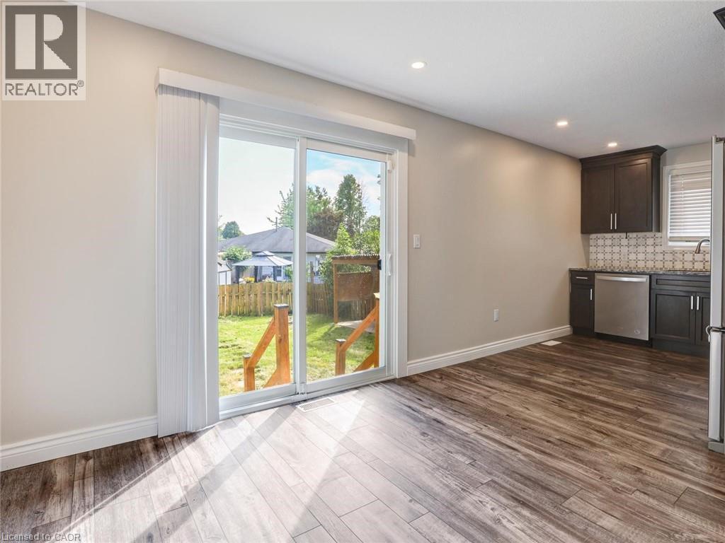 Sliding glass patio doors opening to a backyard with wood-finish flooring, recessed lighting, and a kitchen area featuring dark cabinetry, stainless steel appliances, and a mosaic tile backsplash - 833 Doon Village Road, Kitchener, ON - Indoor