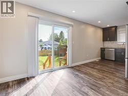 Sliding glass patio doors opening to a backyard with wood-finish flooring, recessed lighting, and a kitchen area featuring dark cabinetry, stainless steel appliances, and a mosaic tile backsplash -