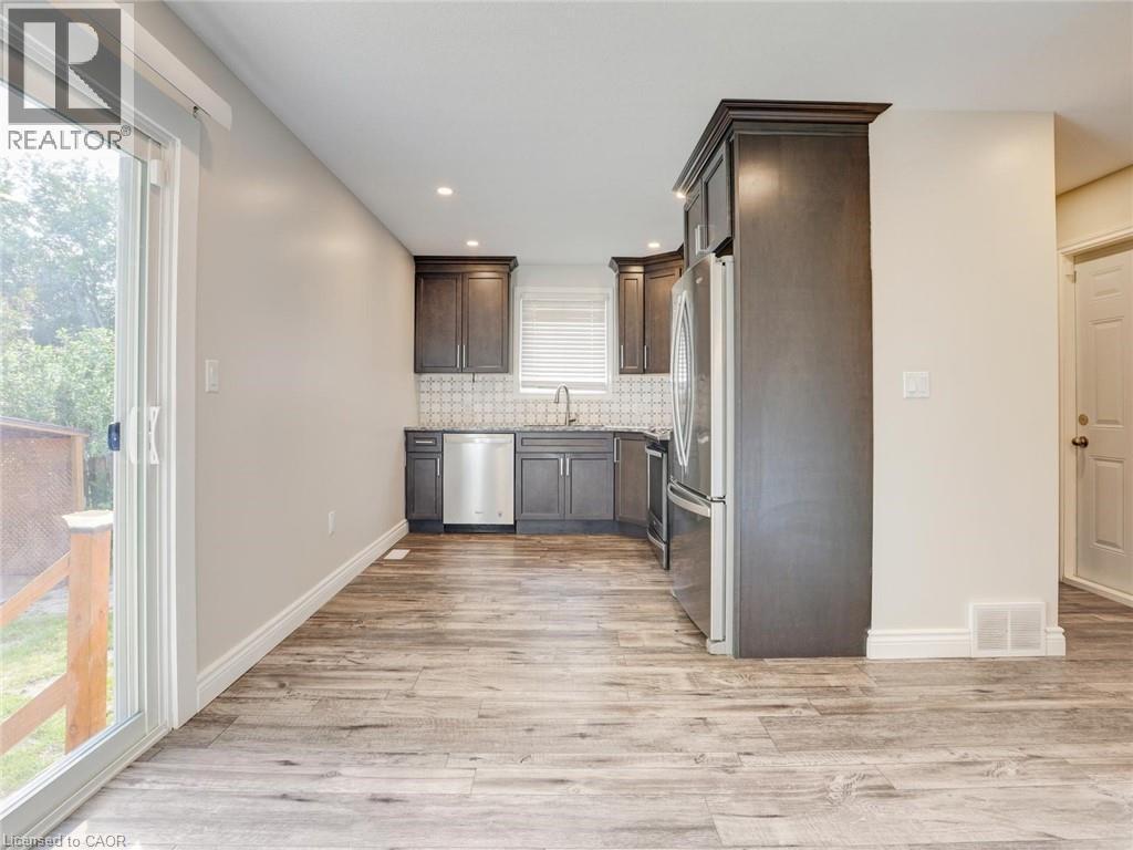 Kitchen with dark wood cabinetry, stainless steel appliances, and a patterned tile backsplash - 833 Doon Village Road, Kitchener, ON - Indoor Photo Showing Kitchen