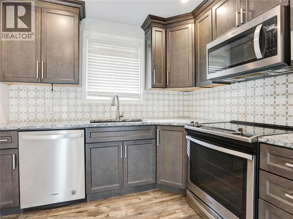 Kitchen featuring stainless steel appliances, grey shaker-style cabinetry, patterned tile backsplash, stone-look countertops, and wood-finish flooring - 833 Doon Village Road, Kitchener, ON - Indoor Photo Showing Kitchen With Upgraded Kitchen