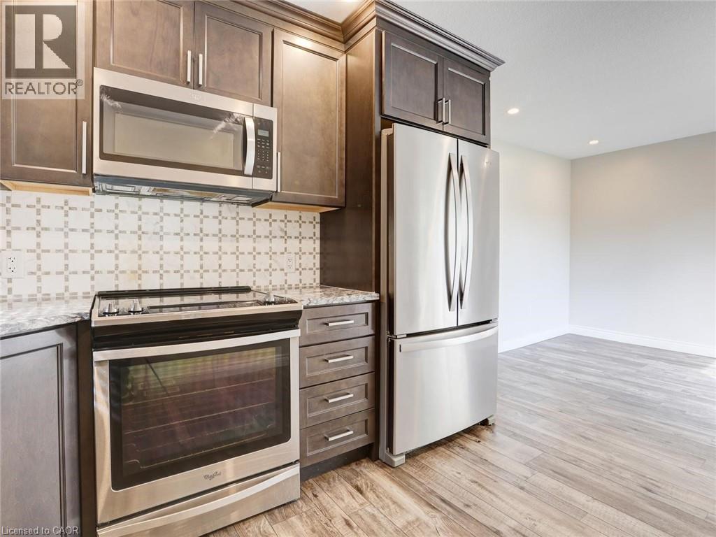 Kitchen featuring stainless steel appliances, wood-finish flooring, dark wood cabinetry, a patterned tile backsplash, and light-toned countertops - 833 Doon Village Road, Kitchener, ON - Indoor Photo Showing Kitchen With Upgraded Kitchen