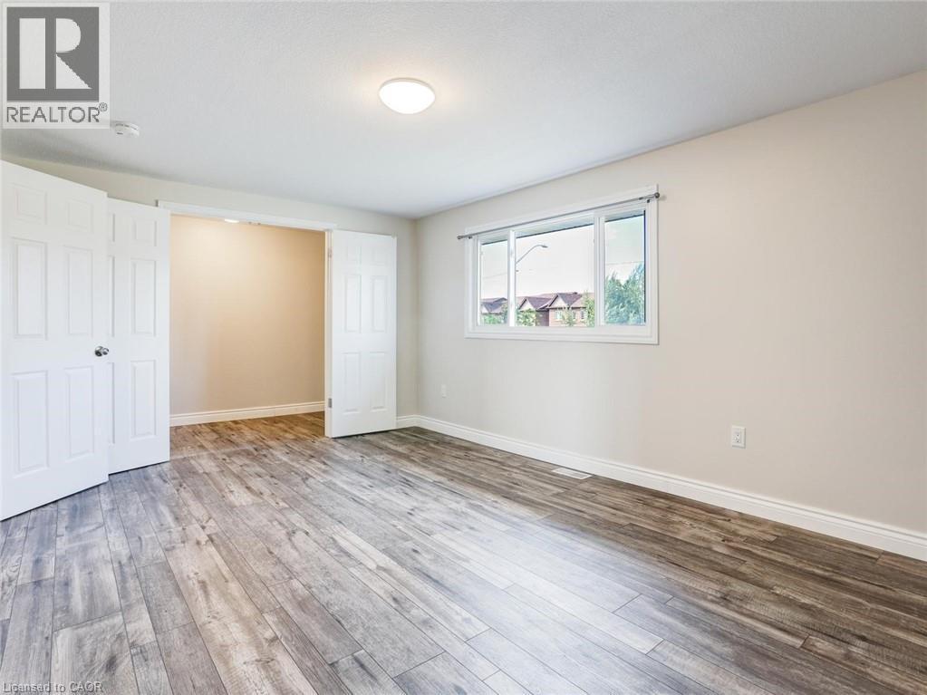 Spacious interior featuring wood-finish flooring, neutral wall tones, a ceiling-mounted light fixture, and a large window with white trim - 833 Doon Village Road, Kitchener, ON - Indoor Photo Showing Other Room