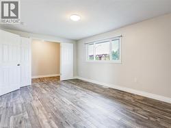 Spacious interior featuring wood-finish flooring, neutral wall tones, a ceiling-mounted light fixture, and a large window with white trim -