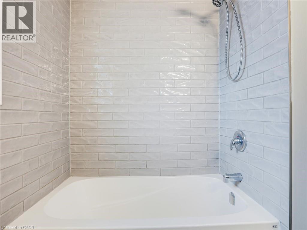Bathtub and shower combination featuring subway tile surround, chrome fixtures, and a white porcelain tub - 833 Doon Village Road, Kitchener, ON - Indoor Photo Showing Bathroom