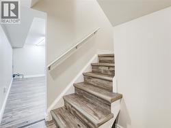 Staircase with wood-finish treads and risers, featuring a white handrail and light neutral wall paint -