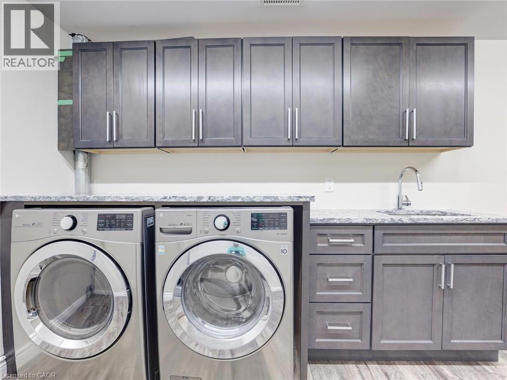Laundry space featuring gray shaker-style cabinetry, a built-in sink with a chrome faucet, light-toned countertops, and wood-finish flooring - 833 Doon Village Road, Kitchener, ON - Indoor Photo Showing Laundry Room