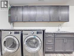 Laundry space featuring gray shaker-style cabinetry, a built-in sink with a chrome faucet, light-toned countertops, and wood-finish flooring -