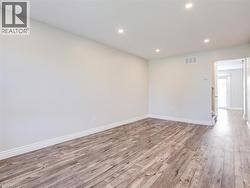 Spacious room with wood-finish flooring, recessed lighting, white baseboards, and neutral wall tones -