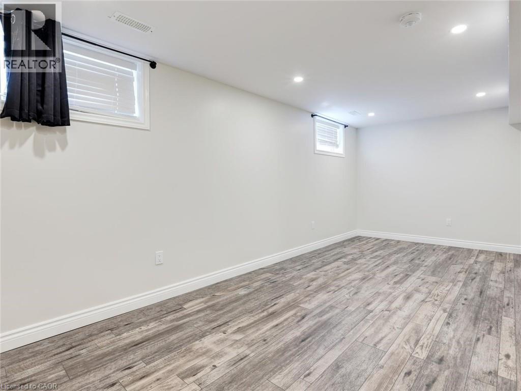Spacious room featuring light gray wood-finish flooring, white walls, and recessed ceiling lighting - 833 Doon Village Road, Kitchener, ON - Indoor