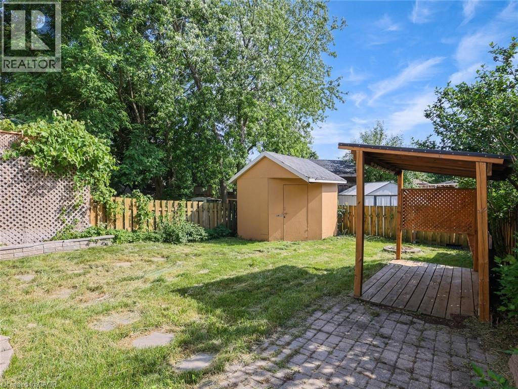 Expansive backyard featuring a covered patio with lattice detailing, a storage shed, a stone paver patio area, and mature perimeter trees - 833 Doon Village Road, Kitchener, ON - Outdoor