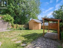 Expansive backyard featuring a covered patio with lattice detailing, a storage shed, a stone paver patio area, and mature perimeter trees -