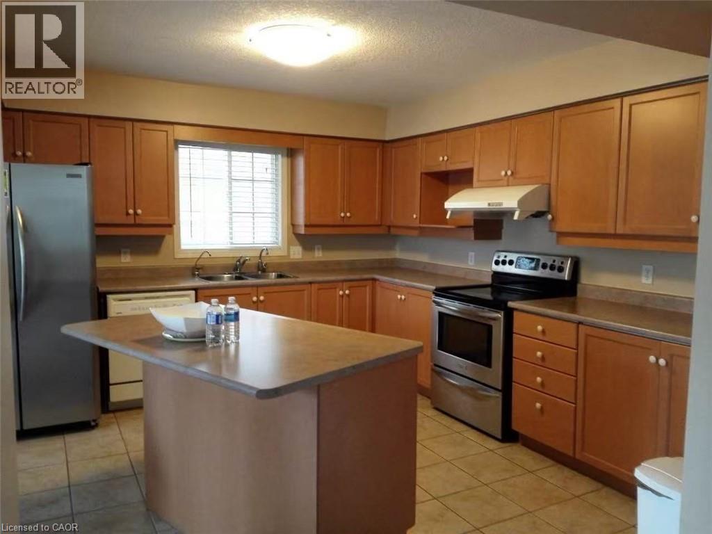 Kitchen featuring wood-finish cabinetry, stainless steel appliances, a center island with an extended countertop, a double basin sink, and tile flooring - 350 Havendale Crescent, Waterloo, ON - Indoor Photo Showing Kitchen With Double Sink