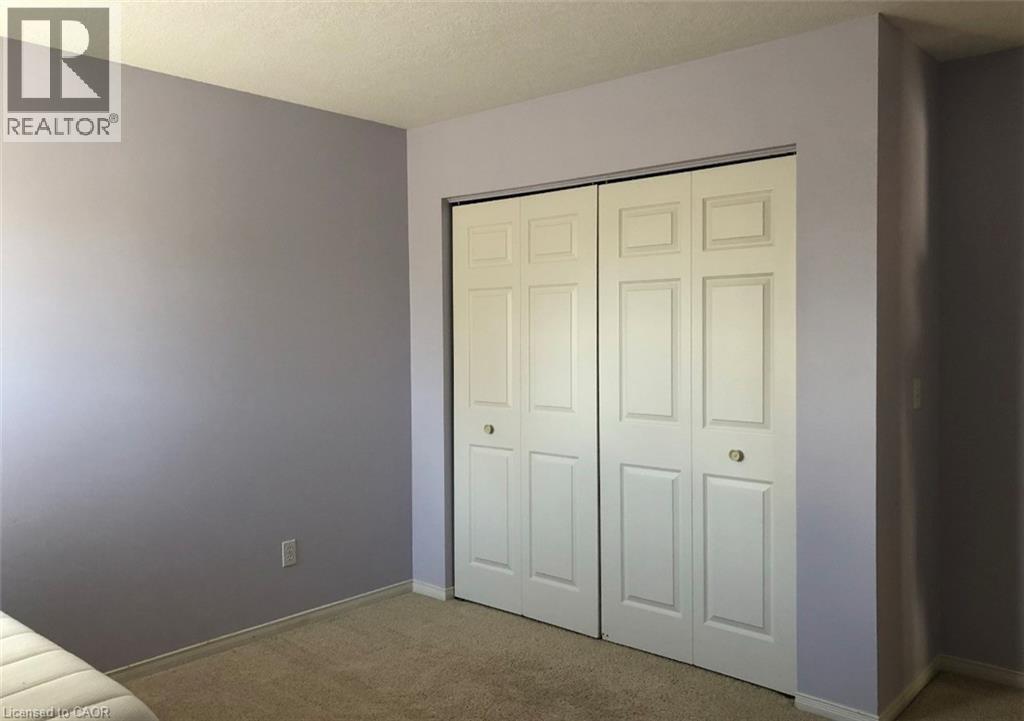 Recessed closet featuring bi-fold panel doors with circular hardware, set against a light purple wall and neutral carpet flooring - 350 Havendale Crescent, Waterloo, ON - Indoor