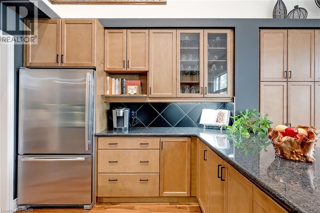 Kitchen featuring natural wood cabinetry, stainless steel refrigerator, dark granite countertops, black tile backsplash, and integrated glass display cabinets - 4285 Couples Crescent, Burlington, ON - Indoor Photo Showing Kitchen