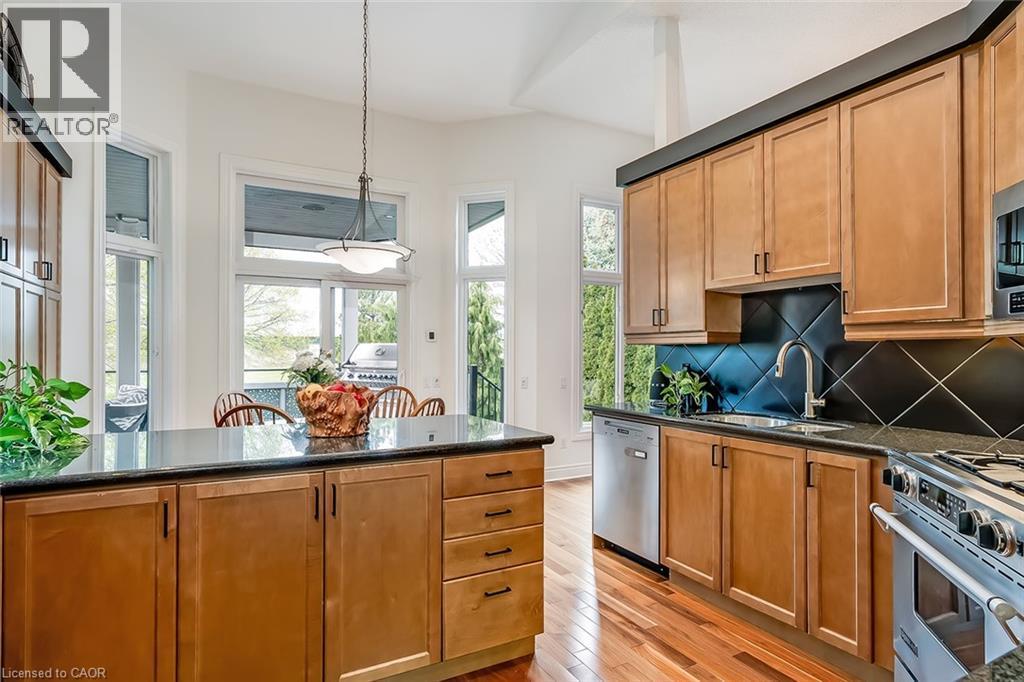 Kitchen featuring wood-finish flooring, light wood cabinetry with dark hardware, dark countertops, and a black diagonal tile backsplash - 4285 Couples Crescent, Burlington, ON - Indoor Photo Showing Kitchen