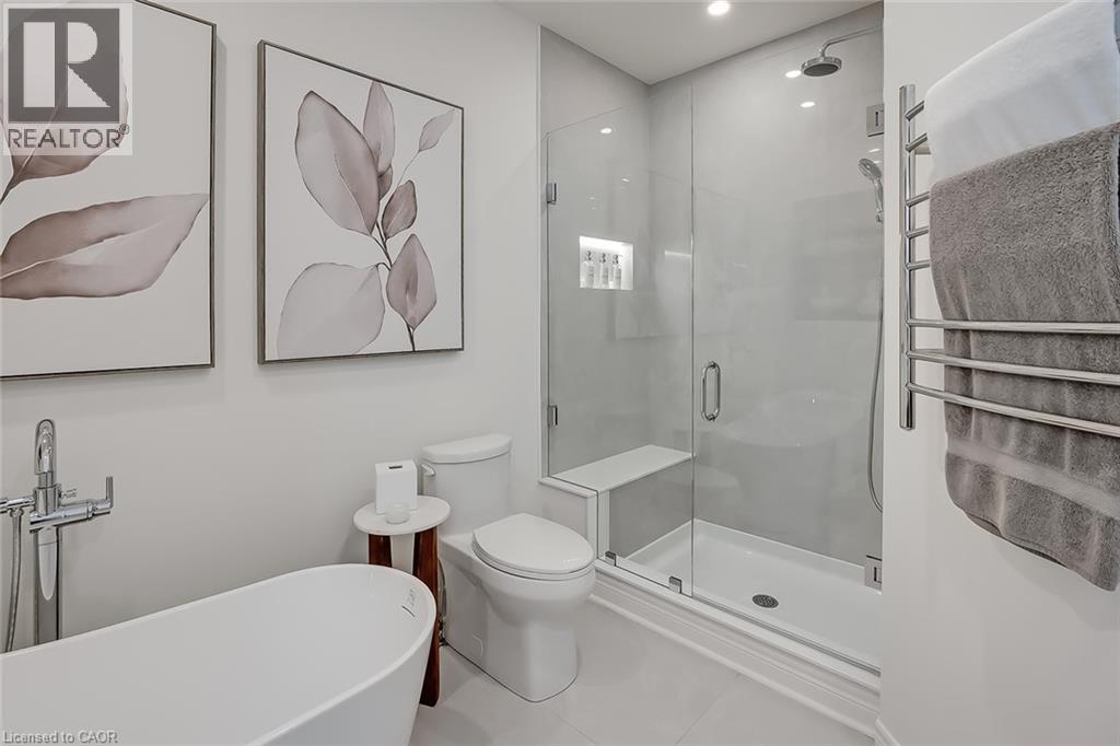 Bathroom featuring a freestanding soaking tub with floor-mounted faucet, a frameless glass shower enclosure with built-in bench and recessed niche, and a wall-mounted towel warmer - 4285 Couples Crescent, Burlington, ON - Indoor Photo Showing Bathroom