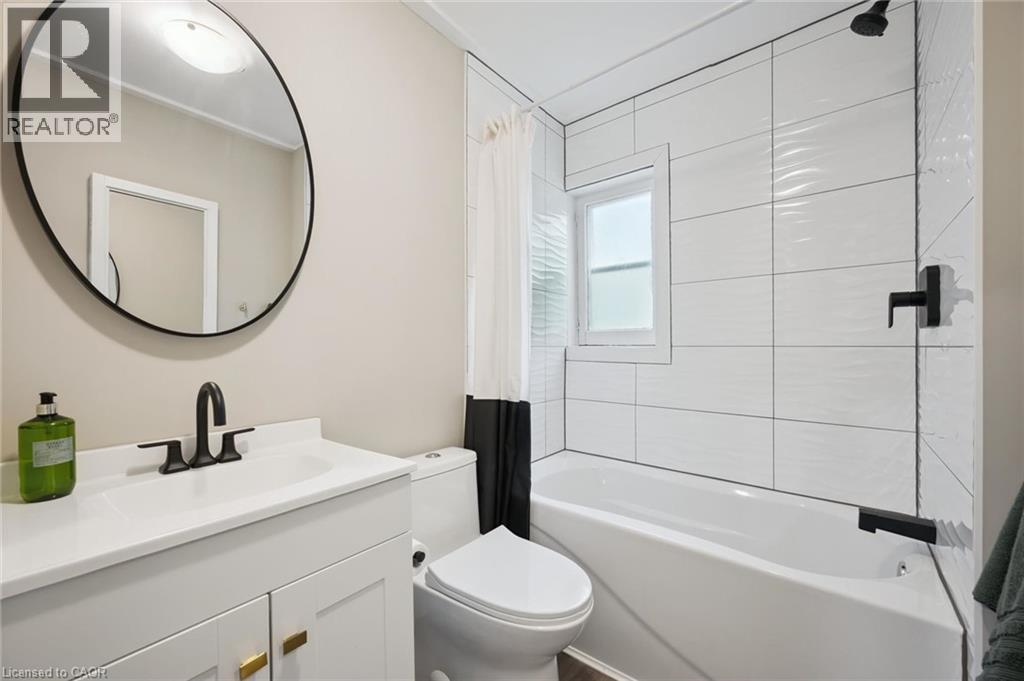 Bathroom featuring a white vanity with gold-tone hardware, a circular mirror, and matte black plumbing fixtures - 15 Gordon Avenue, Kitchener, ON - Indoor Photo Showing Bathroom