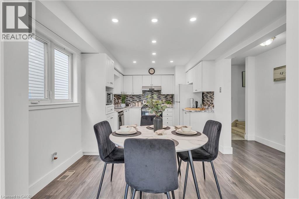 Open-concept kitchen and dining area featuring recessed lighting, white cabinetry, a patterned tile backsplash, stainless steel appliances, and wood-finish flooring - 425 Erinbrook Drive, Kitchener, ON - Indoor Photo Showing Dining Room