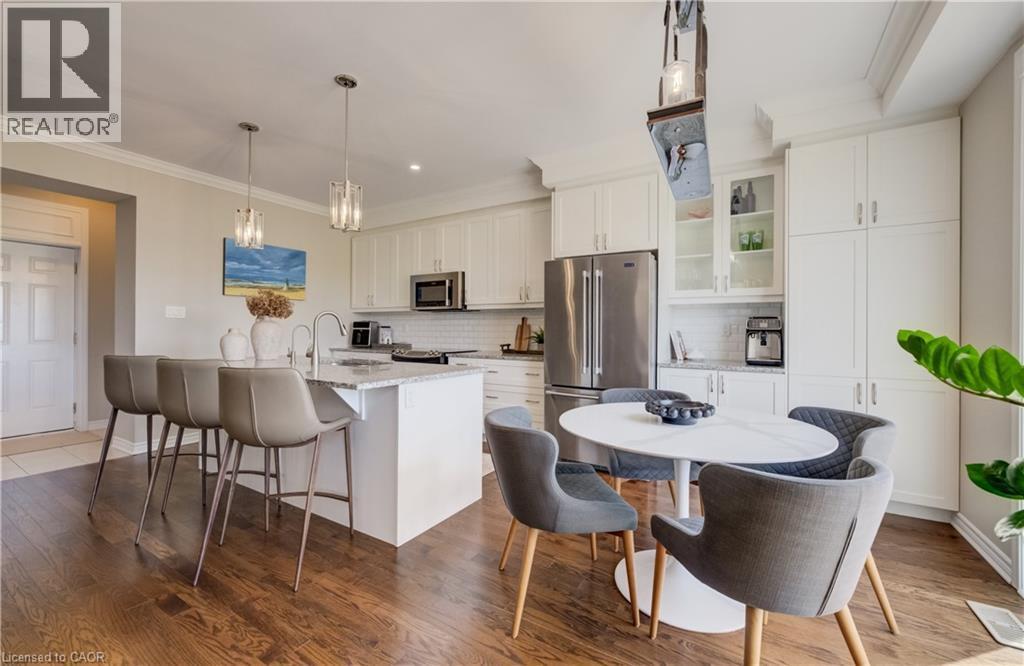 Open-concept kitchen featuring wood-finish flooring, white cabinetry, a large island with seating, pendant lighting, and stainless steel appliances - 19 Shoreacres Drive, Kitchener, ON - Indoor