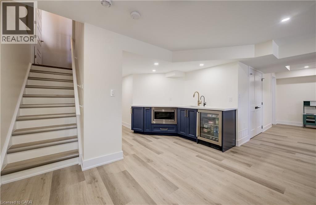 Finished lower level featuring light wood-finish flooring, recessed lighting, and a built-in wet bar with dark cabinetry, integrated microwave, and beverage refrigerator - 19 Shoreacres Drive, Kitchener, ON - Indoor Photo Showing Other Room With Fireplace