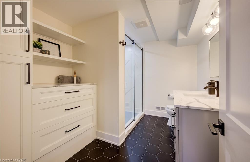 Bathroom featuring a frameless glass shower enclosure, dark hexagonal floor tiles, a vanity with a white countertop, and built-in white cabinetry with open shelving and drawers - 19 Shoreacres Drive, Kitchener, ON - Indoor