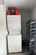Laundry area with dark hardwood / wood-style flooring and stacked washer and clothes dryer -