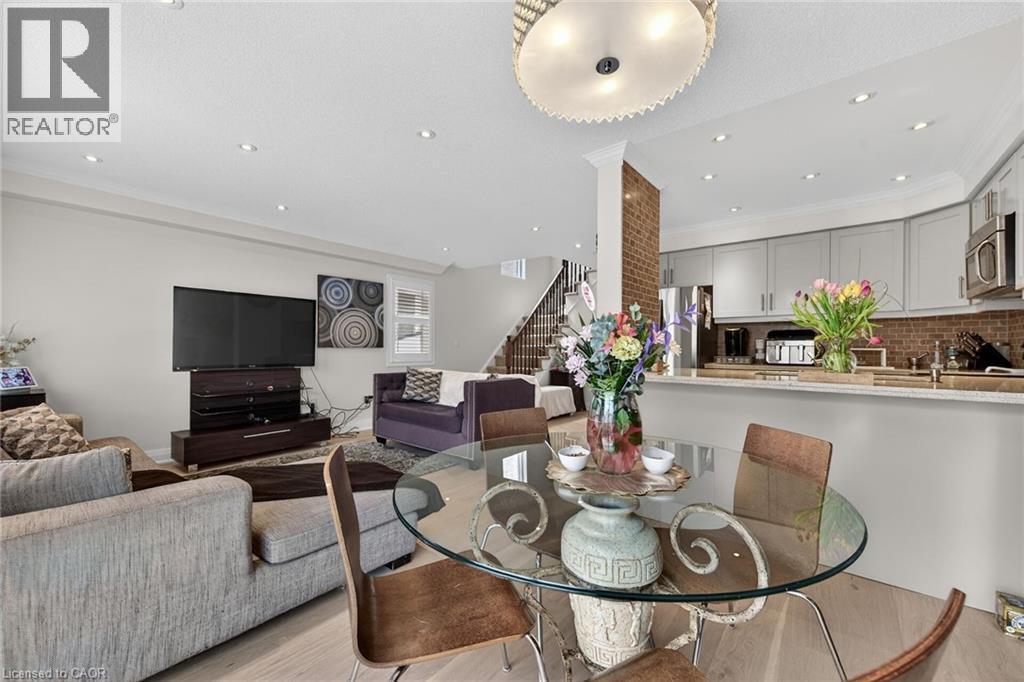 Open-concept living area featuring light wood-finish flooring, recessed lighting, a modern glass-top dining table, and a kitchen with light-colored cabinetry and stainless steel appliances - 4236 Prudham Avenue, Burlington, ON - Indoor Photo Showing Dining Room
