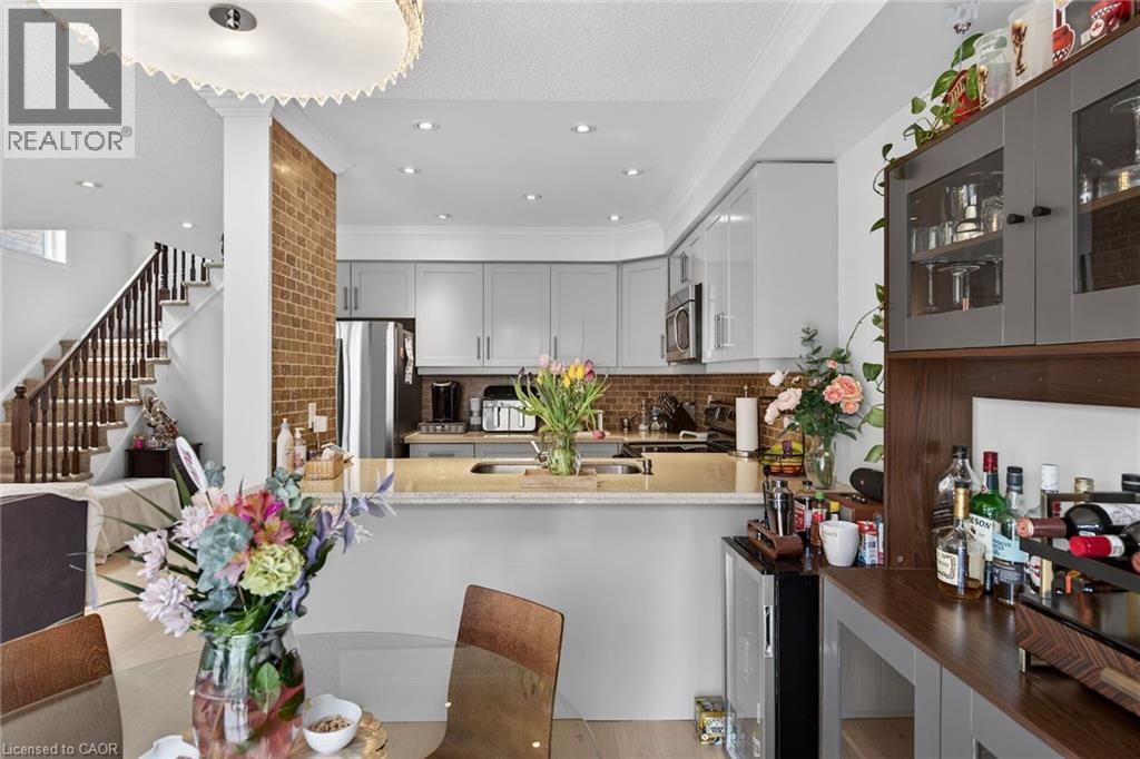 Open-concept kitchen featuring light gray cabinetry, stainless steel appliances, a wood-finish backsplash, and a breakfast bar with a light-toned countertop - 4236 Prudham Avenue, Burlington, ON - Indoor