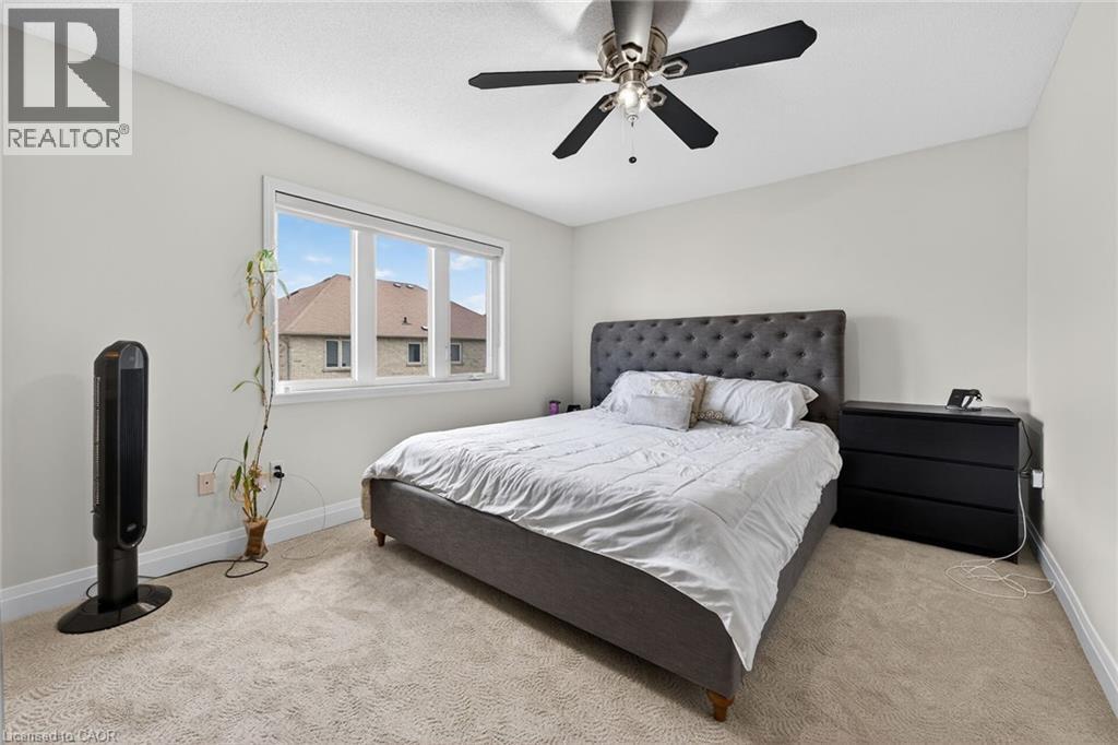 Bright room featuring light-colored carpet flooring, a multi-pane window with white trim, and a ceiling fan with dark blades - 4236 Prudham Avenue, Burlington, ON - Indoor Photo Showing Bedroom
