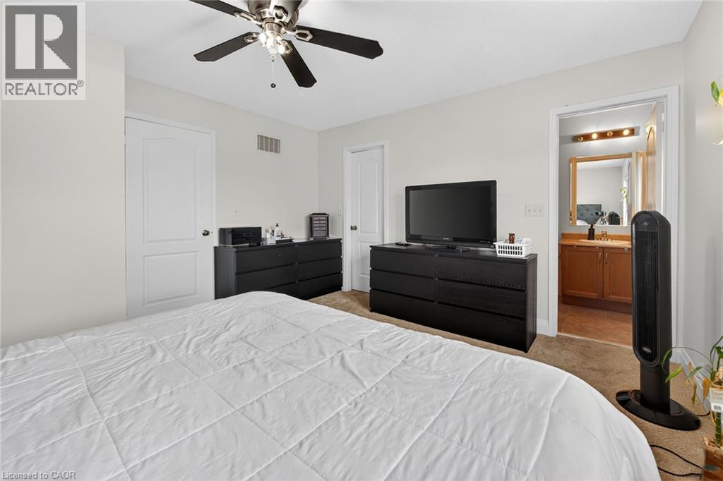 Carpeted bedroom featuring a ceiling fan, white paneled doors, and access to a bathroom with a wood-finish vanity and mirror - 4236 Prudham Avenue, Burlington, ON - Indoor Photo Showing Bedroom