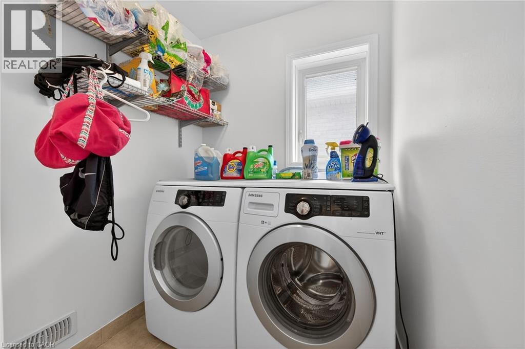 Dedicated laundry area featuring a front-loading washer and dryer set, white walls, light-toned tile flooring, and a window - 4236 Prudham Avenue, Burlington, ON - Indoor Photo Showing Laundry Room