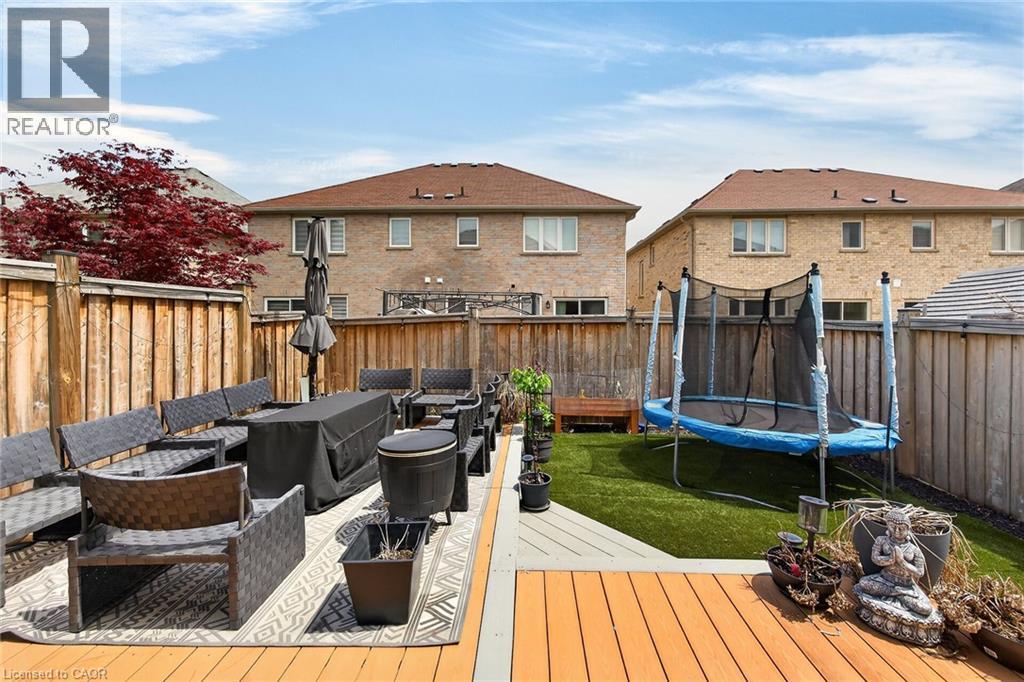 Expansive outdoor living area featuring a wooden deck, artificial turf, a spacious patio area, perimeter wooden fencing, and mature landscaping - 4236 Prudham Avenue, Burlington, ON - Outdoor With Deck Patio Veranda With Exterior