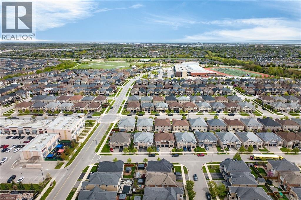 Expansive aerial perspective showcasing a residential development with numerous single-family homes, commercial structures, and a large recreational field - 4236 Prudham Avenue, Burlington, ON - Outdoor With View