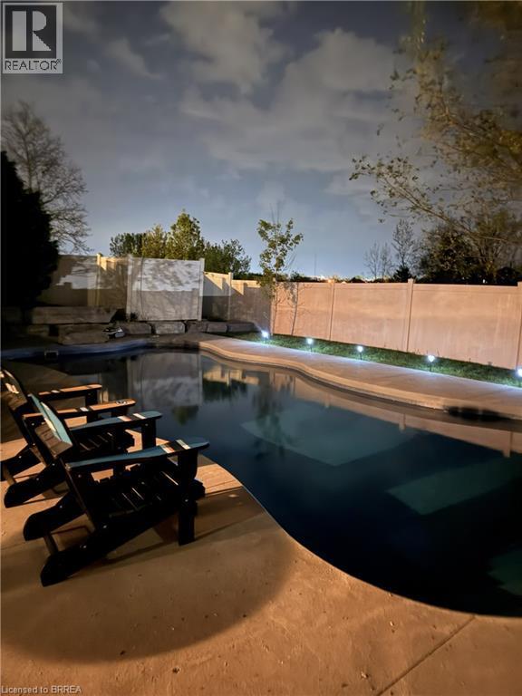 Curved swimming pool with integrated steps, surrounded by concrete decking and perimeter lighting - 34 Pace Avenue, Brantford, ON - Outdoor