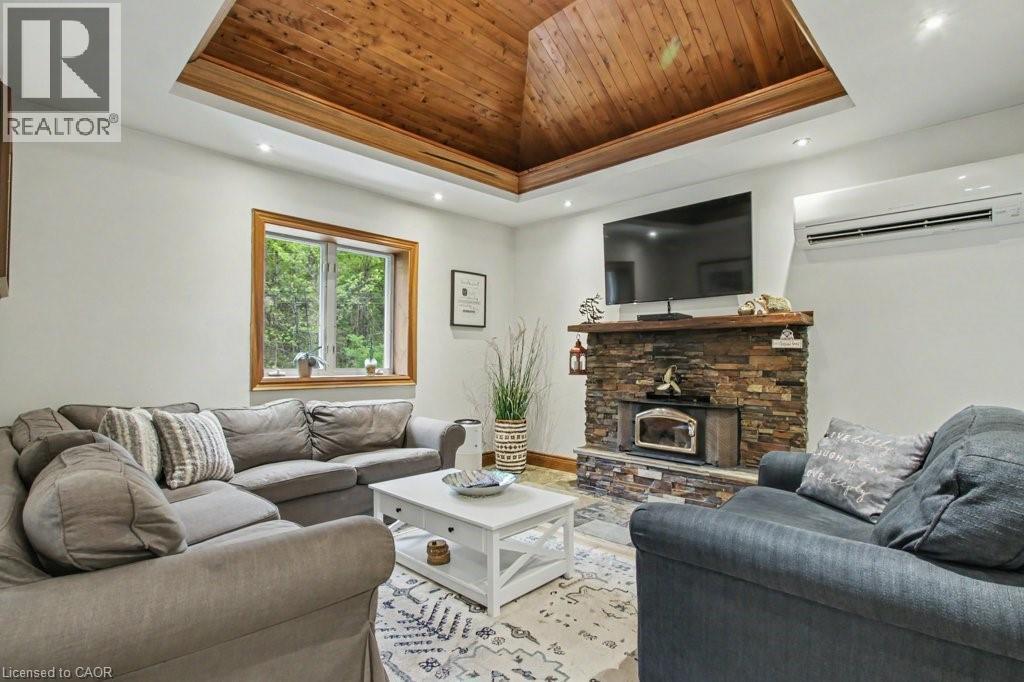 Living area featuring a tray ceiling with wood-finish paneling, a stone-front fireplace with a wood mantel, a large window with wood trim, and recessed lighting - 1333 Hidden Valley Road, Burlington, ON - Indoor