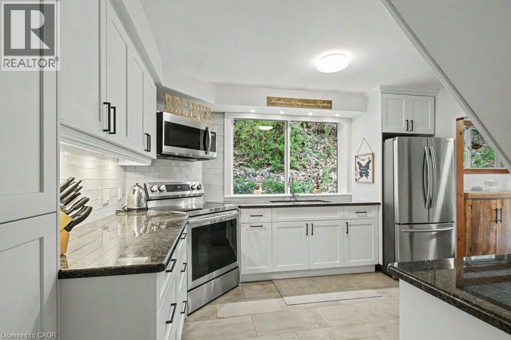 Modern kitchen featuring white cabinetry, dark countertops, and stainless steel appliances - 1333 Hidden Valley Road, Burlington, ON - Indoor Photo Showing Laundry Room