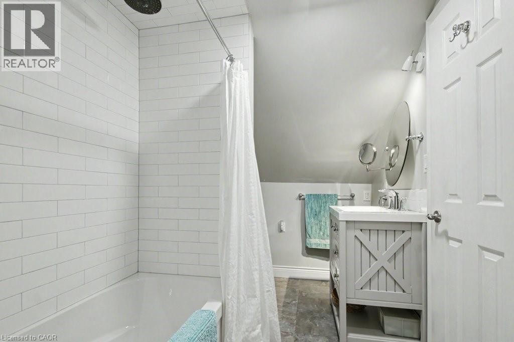 Bathroom featuring a white subway tile shower surround, a built-in tub, a light gray vanity with X-panel detailing, a circular mirror, and wall-mounted lighting - 1333 Hidden Valley Road, Burlington, ON - Indoor Photo Showing Bathroom