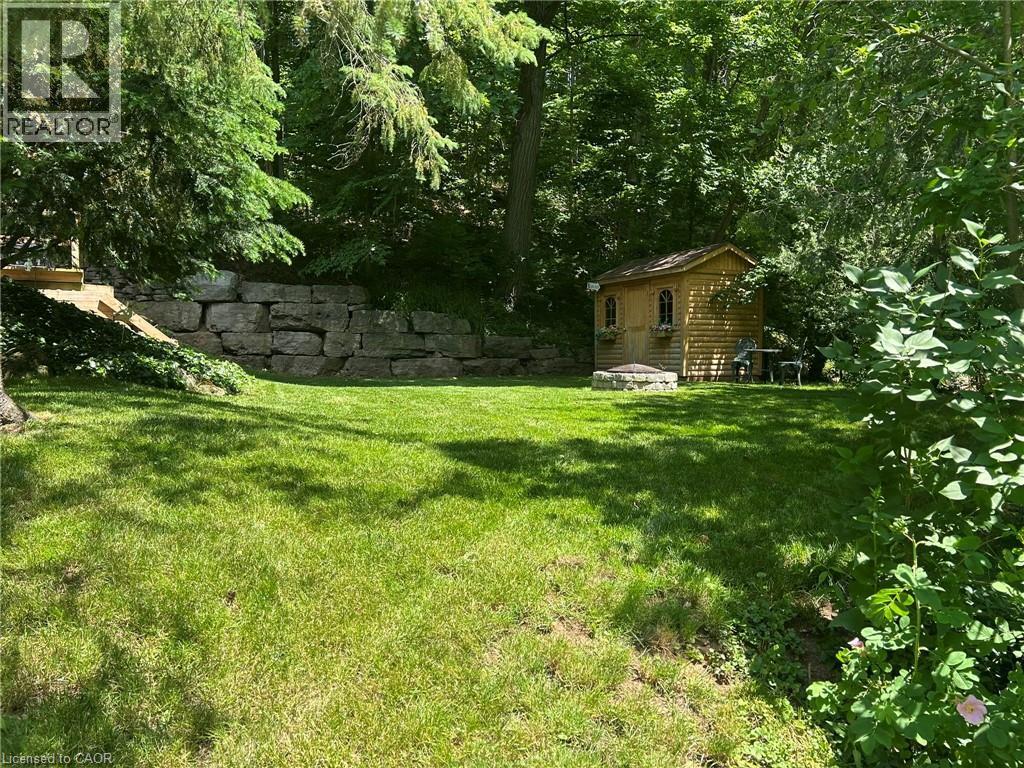 Expansive grassy yard featuring a decorative wood-sided shed with arched window details, a circular stone fire pit, and a natural stone retaining wall - 1333 Hidden Valley Road, Burlington, ON - Indoor Photo Showing Bedroom