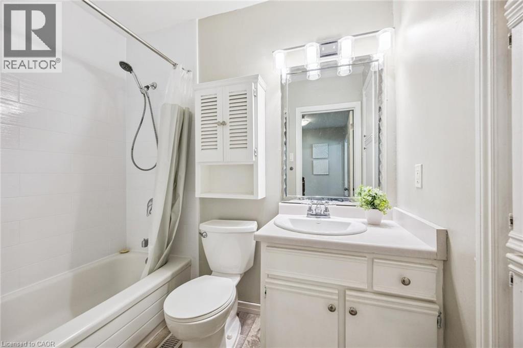 Bathroom featuring a vanity with an integrated sink, a rectangular mirror with integrated lighting, a toilet, a built-in tub with a shower fixture, and white wall tiling - 87 Barbara Crescent, Kitchener, ON - Indoor Photo Showing Bathroom