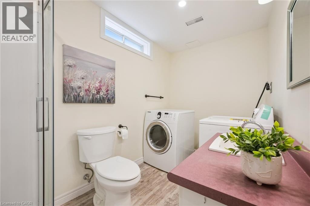Utility room featuring a glass shower enclosure, white toilet, and wood-finish flooring - 87 Barbara Crescent, Kitchener, ON - Indoor Photo Showing Laundry Room