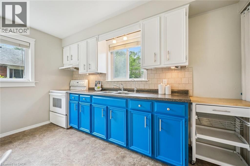 Kitchen featuring two windows, white upper cabinetry, blue lower cabinetry, stone-finish countertops, and a tiled backsplash - 87 Barbara Crescent, Kitchener, ON - Indoor Photo Showing Kitchen With Double Sink
