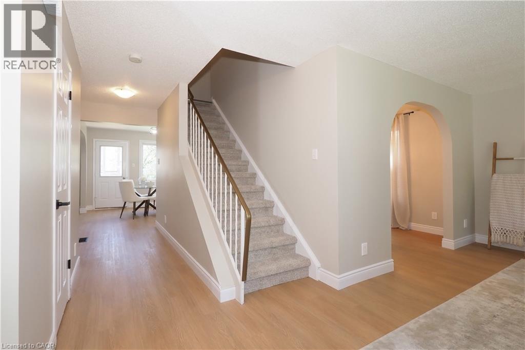 Foyer featuring wood-finish flooring, a carpeted staircase with white balusters, and an arched doorway leading to an additional space - 27 Scenic Wood Crescent, Kitchener, ON - Indoor Photo Showing Other Room