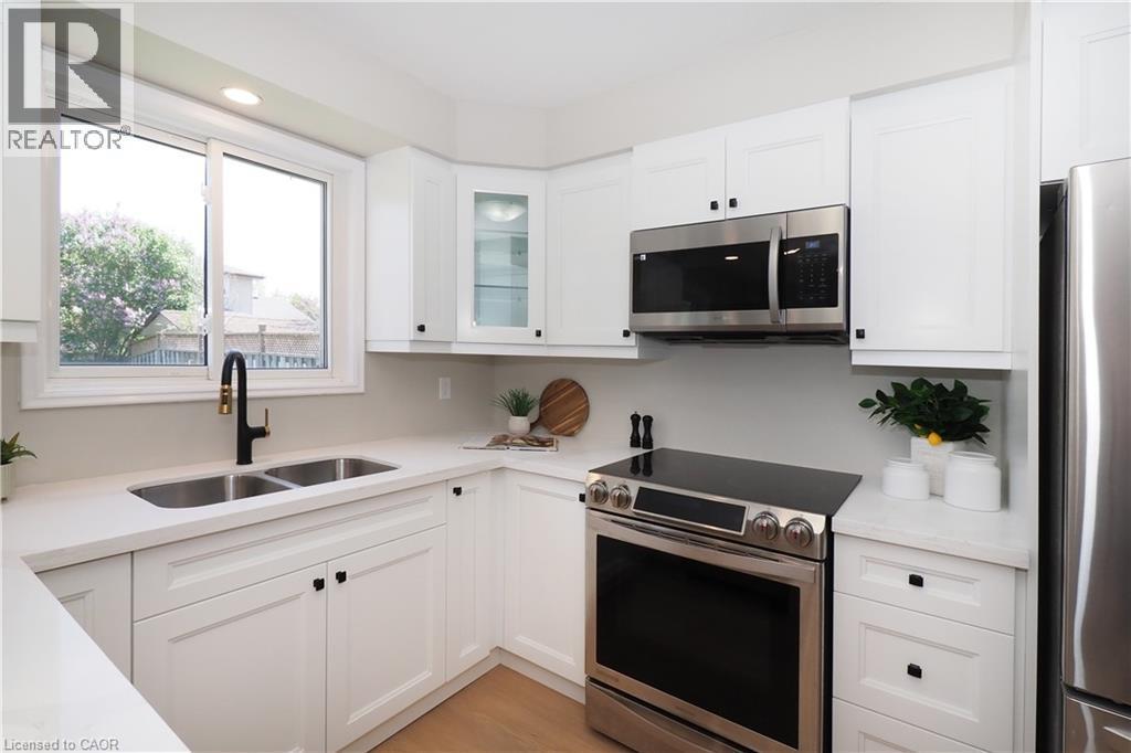 White shaker cabinetry with black hardware, stainless steel appliances, a dual basin undermount sink with a matte black faucet, quartz countertops, and wood-finish flooring - 27 Scenic Wood Crescent, Kitchener, ON - Indoor Photo Showing Kitchen With Double Sink