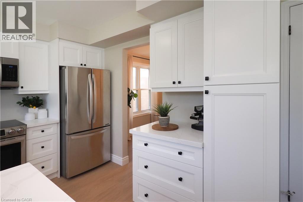 Bright kitchen featuring white shaker cabinetry with black hardware, stainless steel appliances, light wood-finish flooring, and white countertops - 27 Scenic Wood Crescent, Kitchener, ON - Indoor Photo Showing Kitchen
