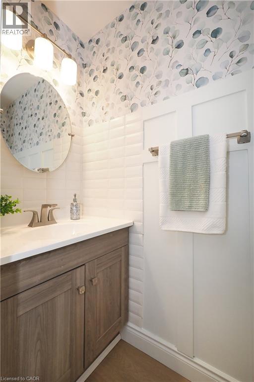 Bathroom featuring a wood-finish vanity with a white countertop, an oval mirror, and a three-light vanity fixture - 27 Scenic Wood Crescent, Kitchener, ON - Indoor Photo Showing Bathroom