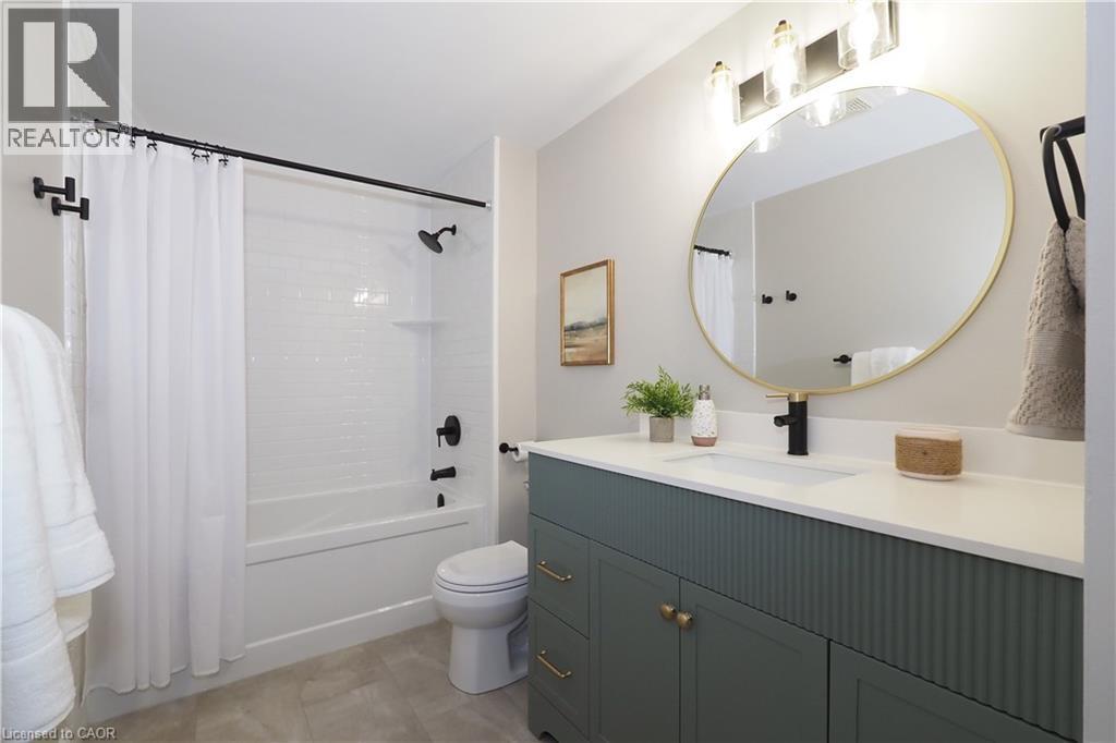 Contemporary bathroom featuring a dark green vanity with brass hardware, a gold-framed circular mirror, and a white countertop with an integrated sink - 27 Scenic Wood Crescent, Kitchener, ON - Indoor Photo Showing Bathroom